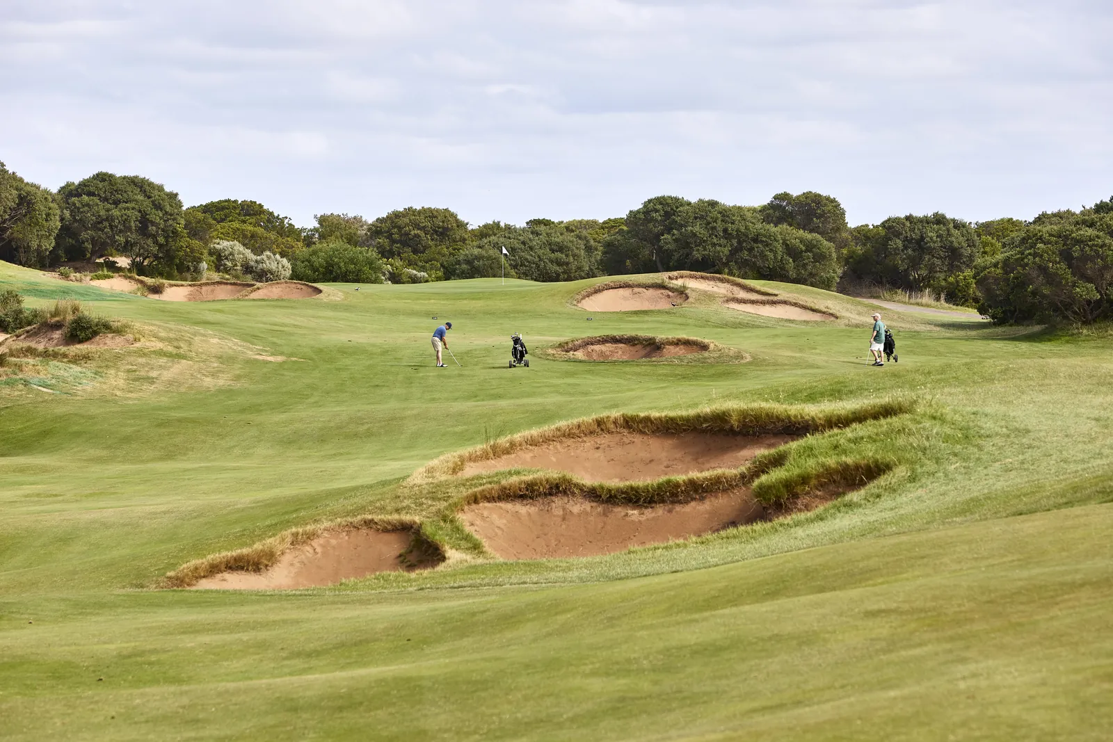 Golfers on a fairway beside deep bunkers at 13th Beach Golf Links