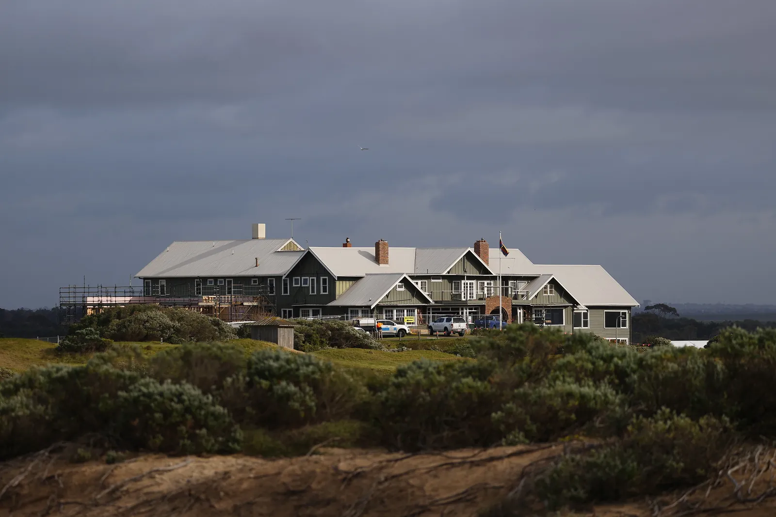 The Barwon Heads Golf Club clubhouse across coastal dune scrub under a stormy sky