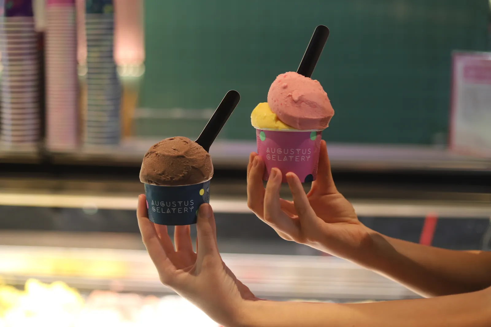 Two cups of gelato held up in front of the cabinet