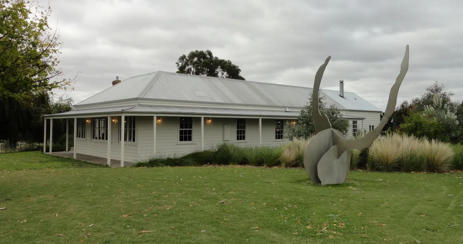 The white weatherboard farmhouse that houses Brae restaurant, with a verandah and a tall metal sculpture on the lawn