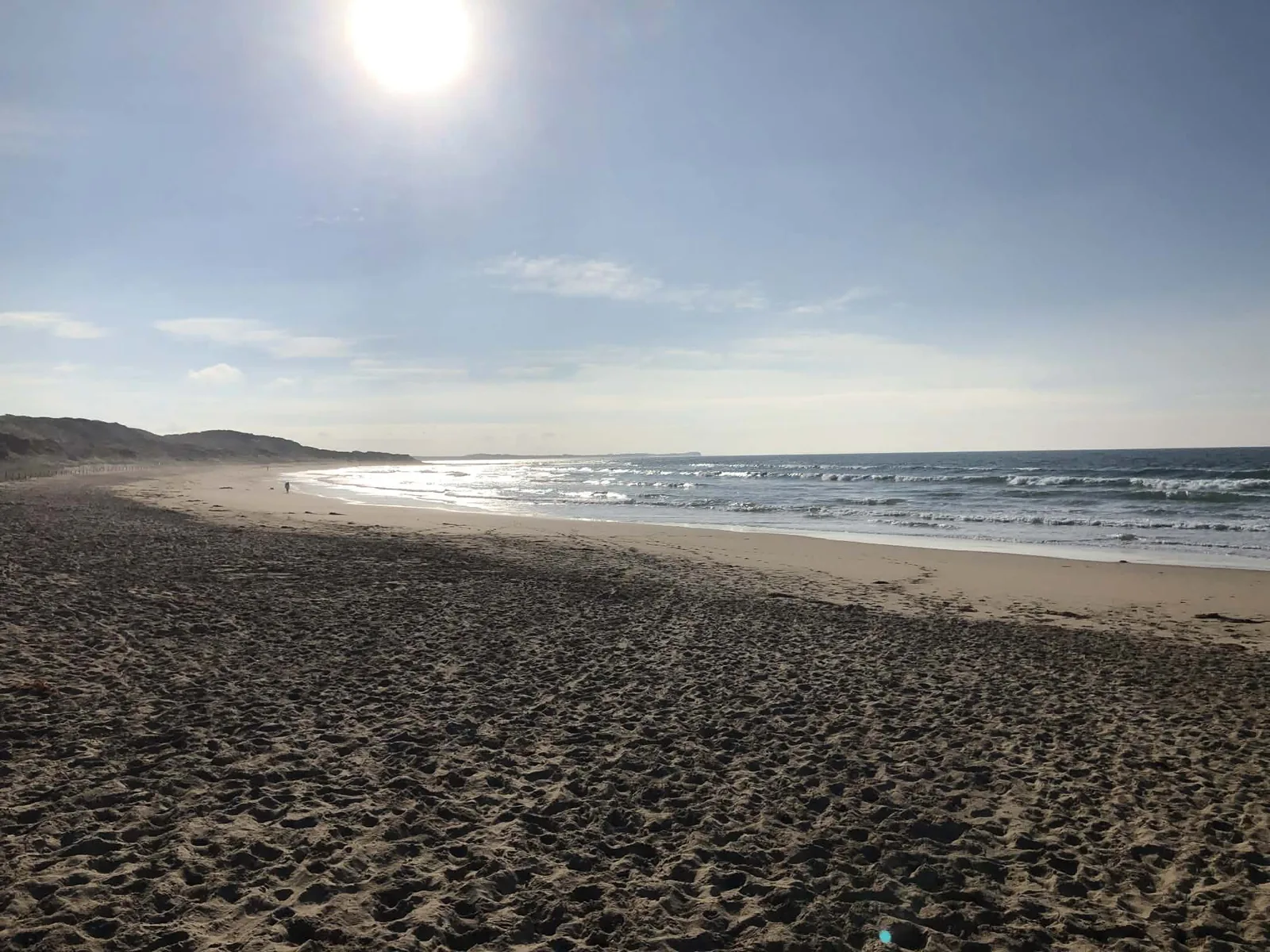 A wide sandy beach with dunes on the left and small waves, at Bancoora Beach near Breamlea