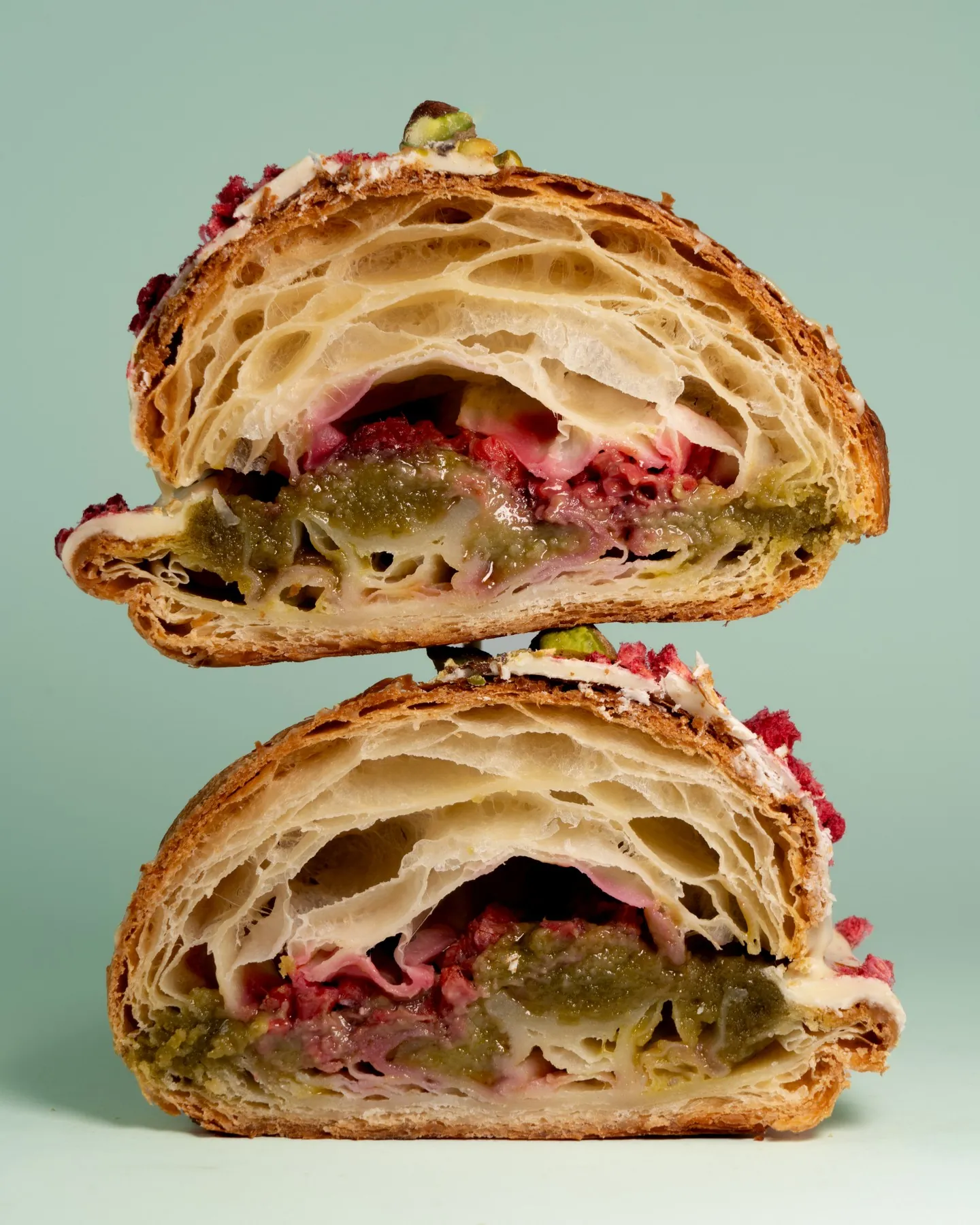 A raspberry and pistachio croissant cut in half to show the filling