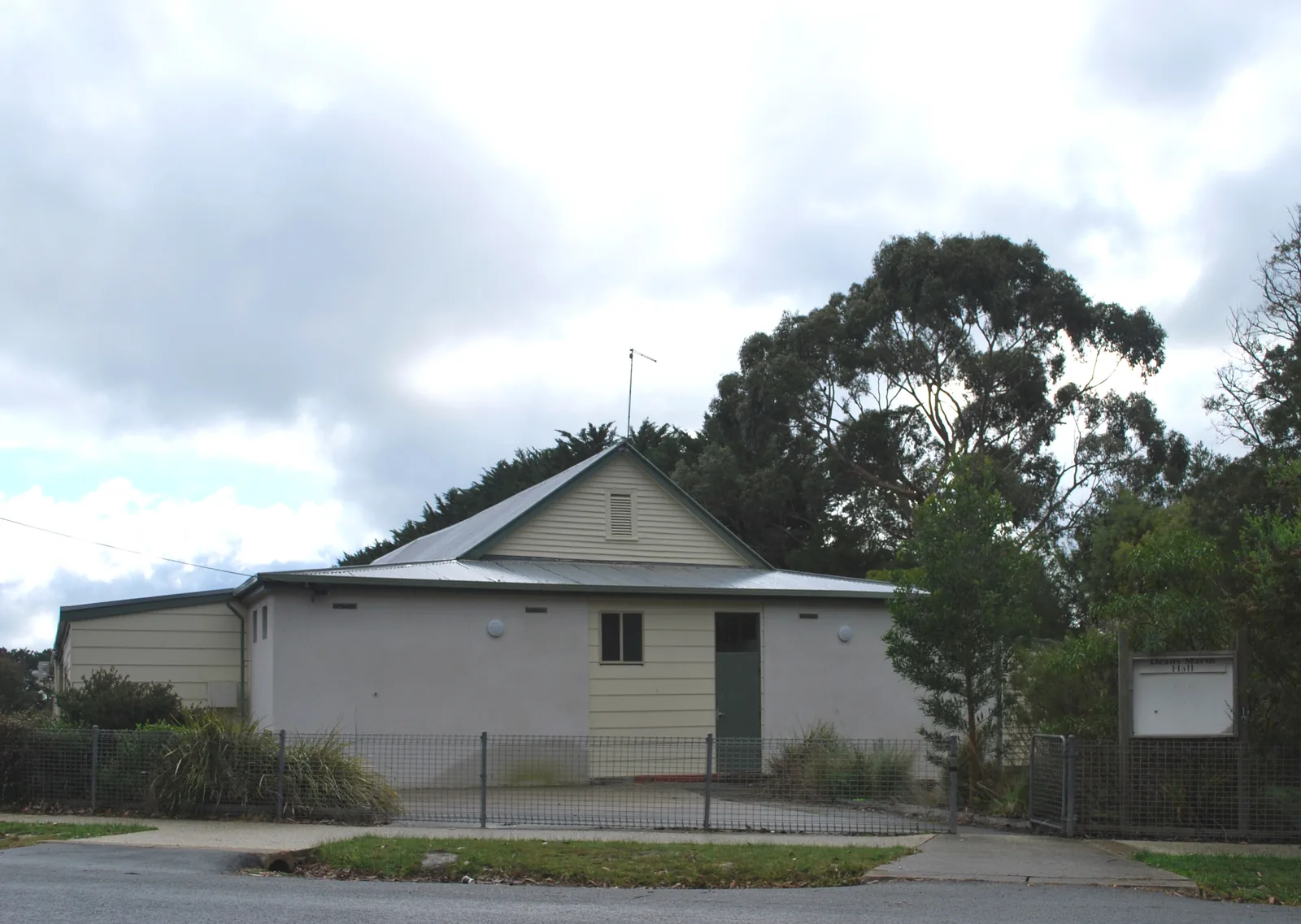 Deans Marsh Public Hall, a low hall behind a wire fence, seen from the street
