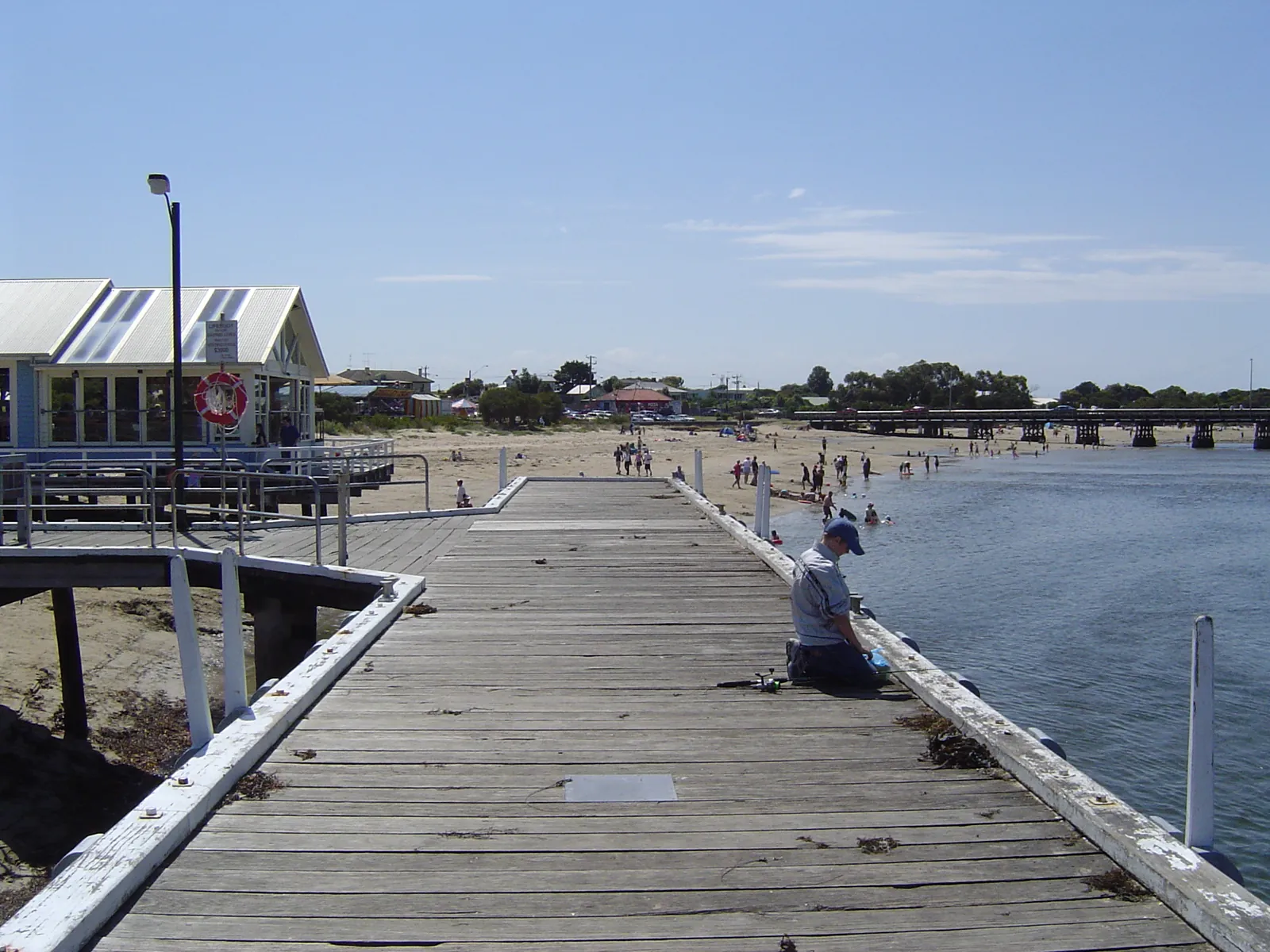 A man fishing off the timber pier at Barwon Heads, with the beach and the old jetty behind