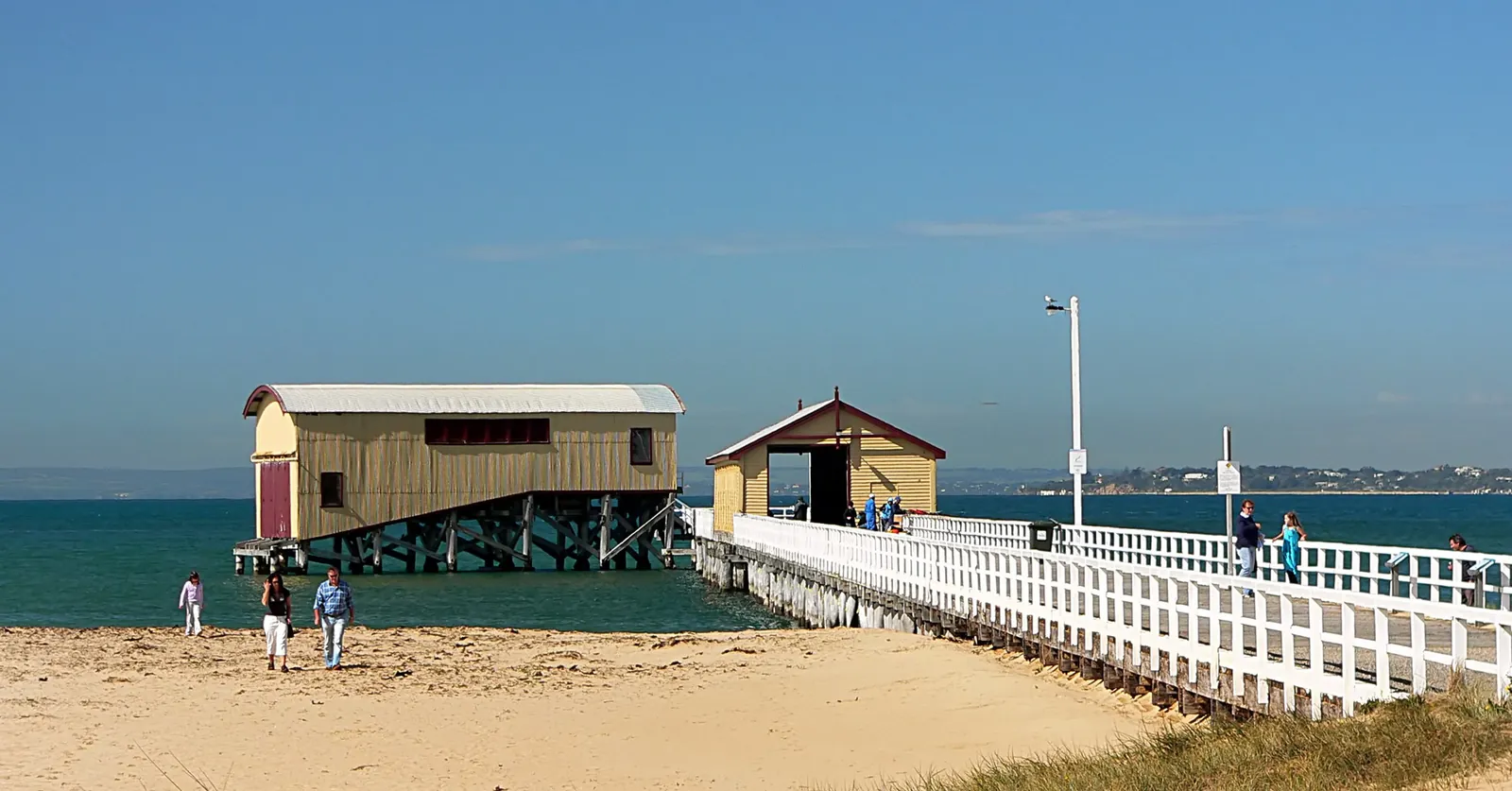 The white timber pier and the old lifeboat shed at Queenscliff, with people walking on the beach
