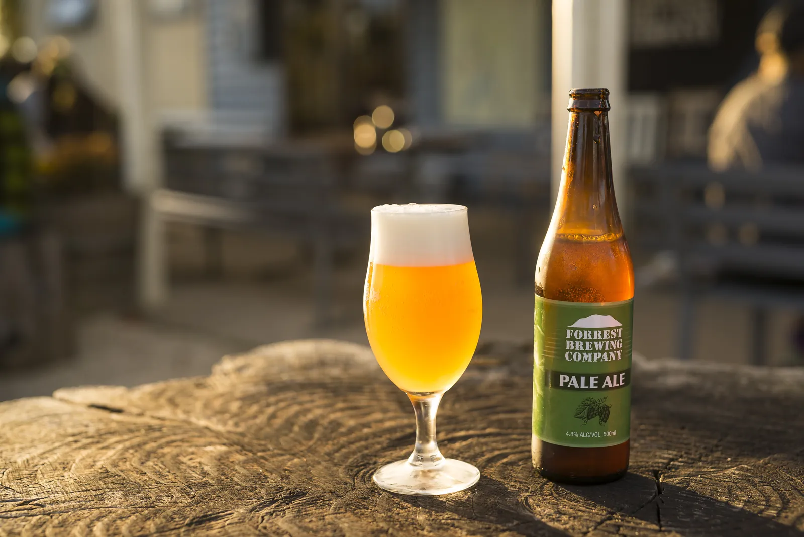 A glass of Forrest pale ale beside a bottle on a timber stump table