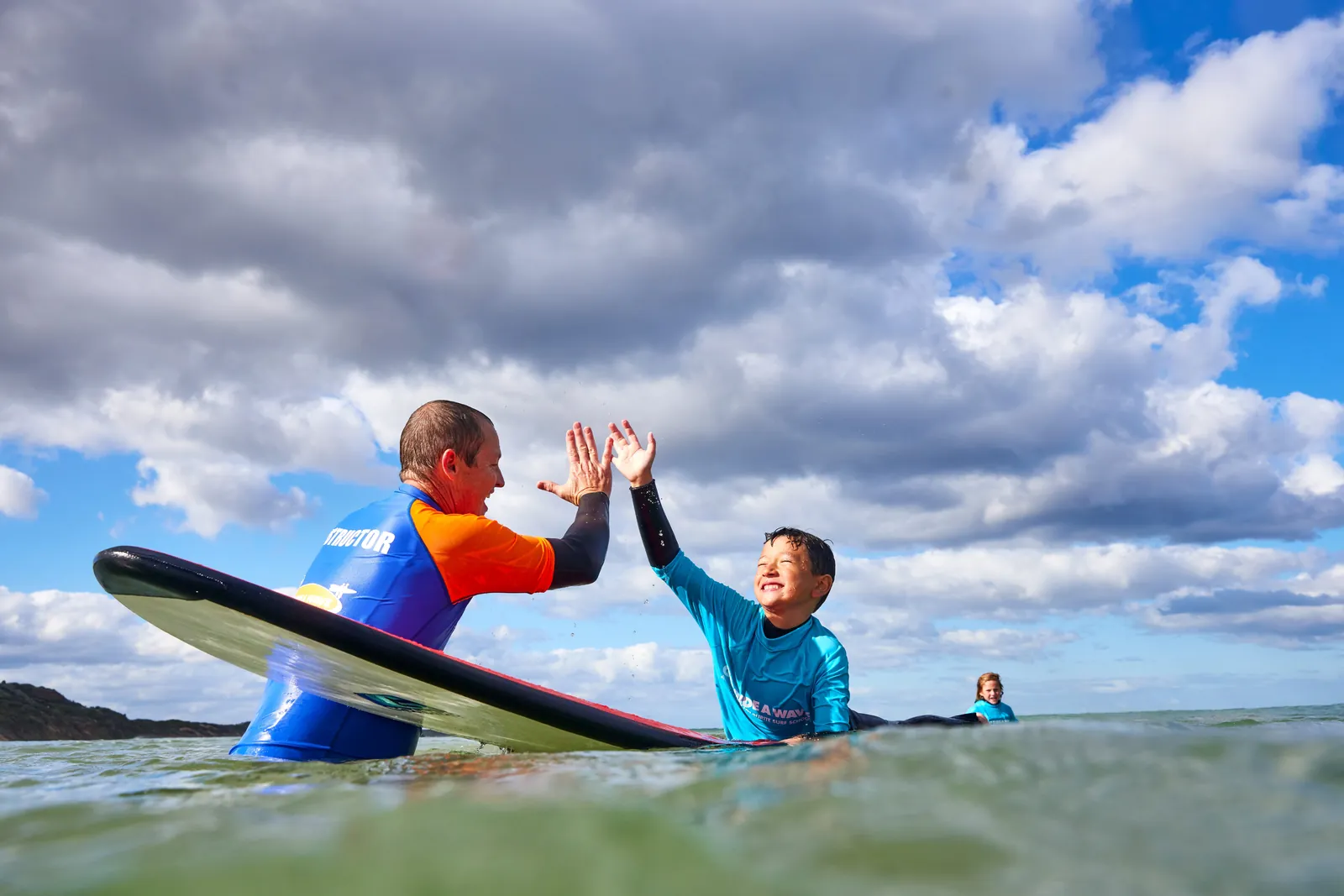 A Go Ride a Wave instructor high-fiving a young surfer in the water during a lesson