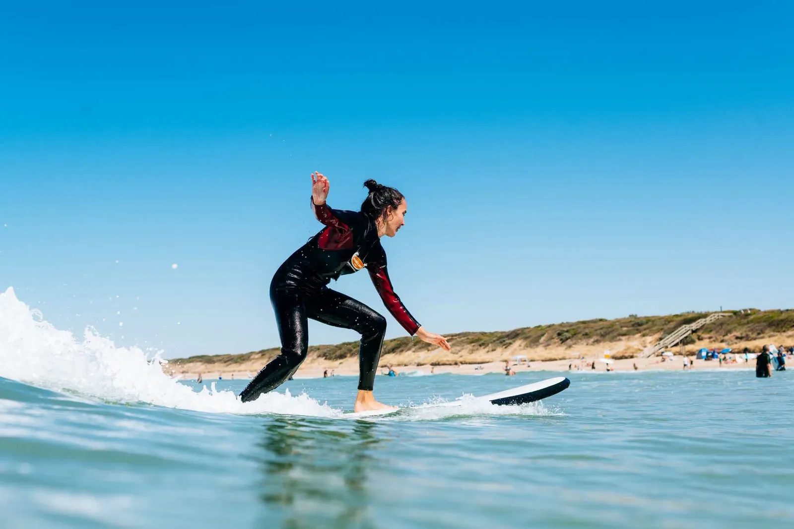 A learner standing up on a soft-top board and riding a small wave
