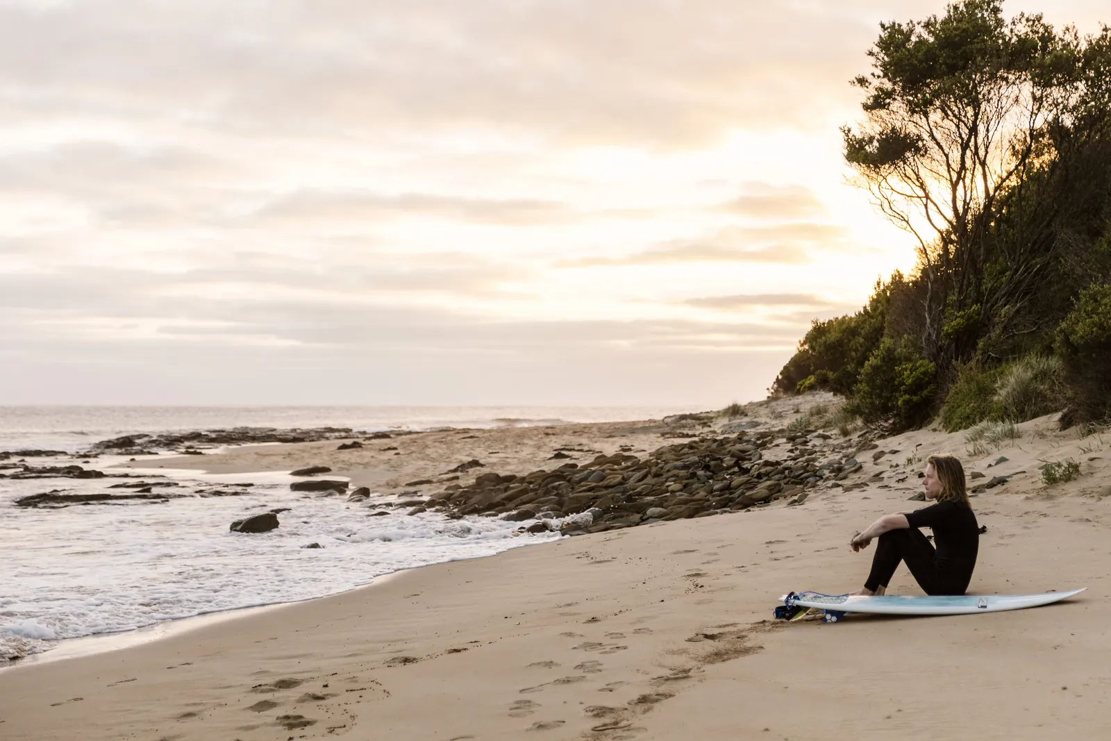 A surfer sitting on the beach at Kennett River in the early light