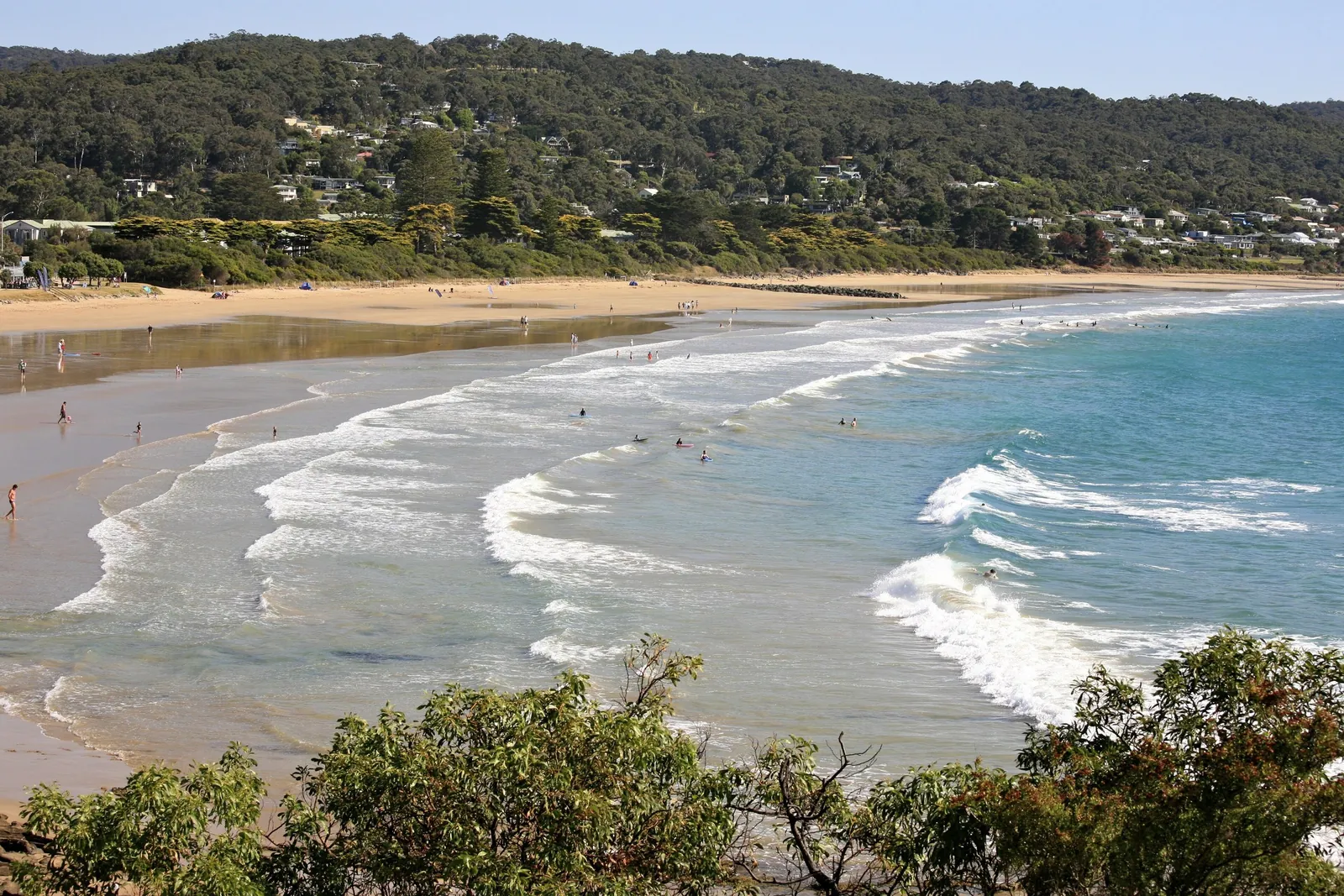 Waves rolling onto Lorne's main beach in summer with the town on the hills behind