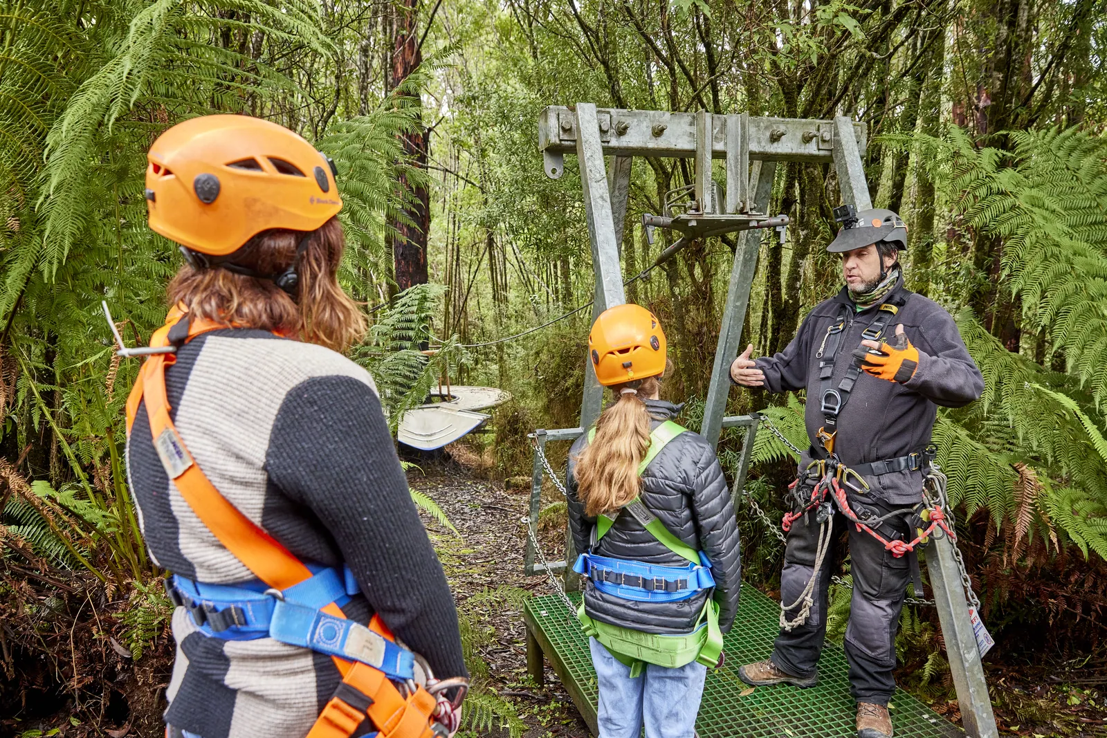A guide helping zipline visitors with their helmets and harnesses in the forest