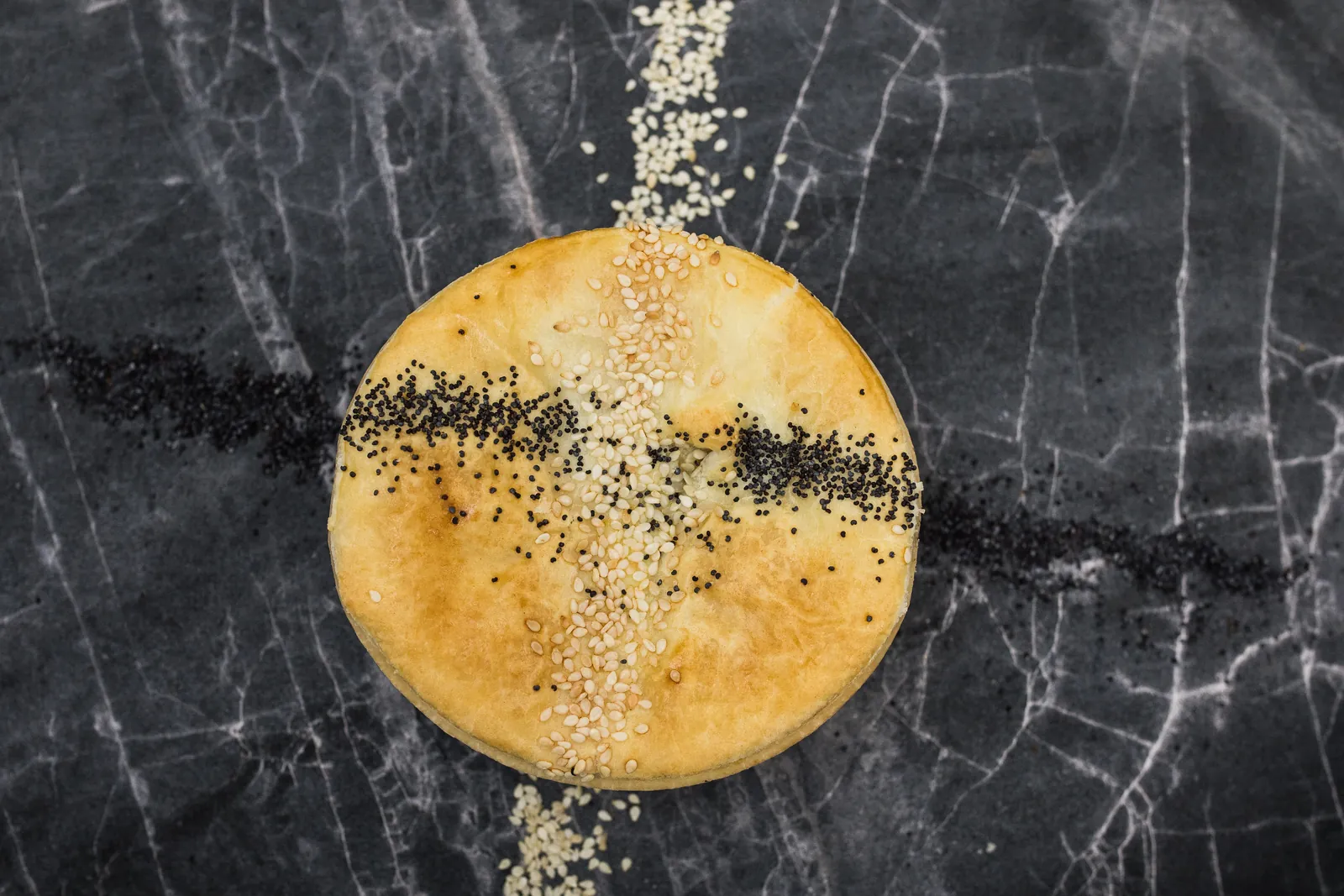 A round Routley's pie topped with sesame and poppy seeds, on dark marble