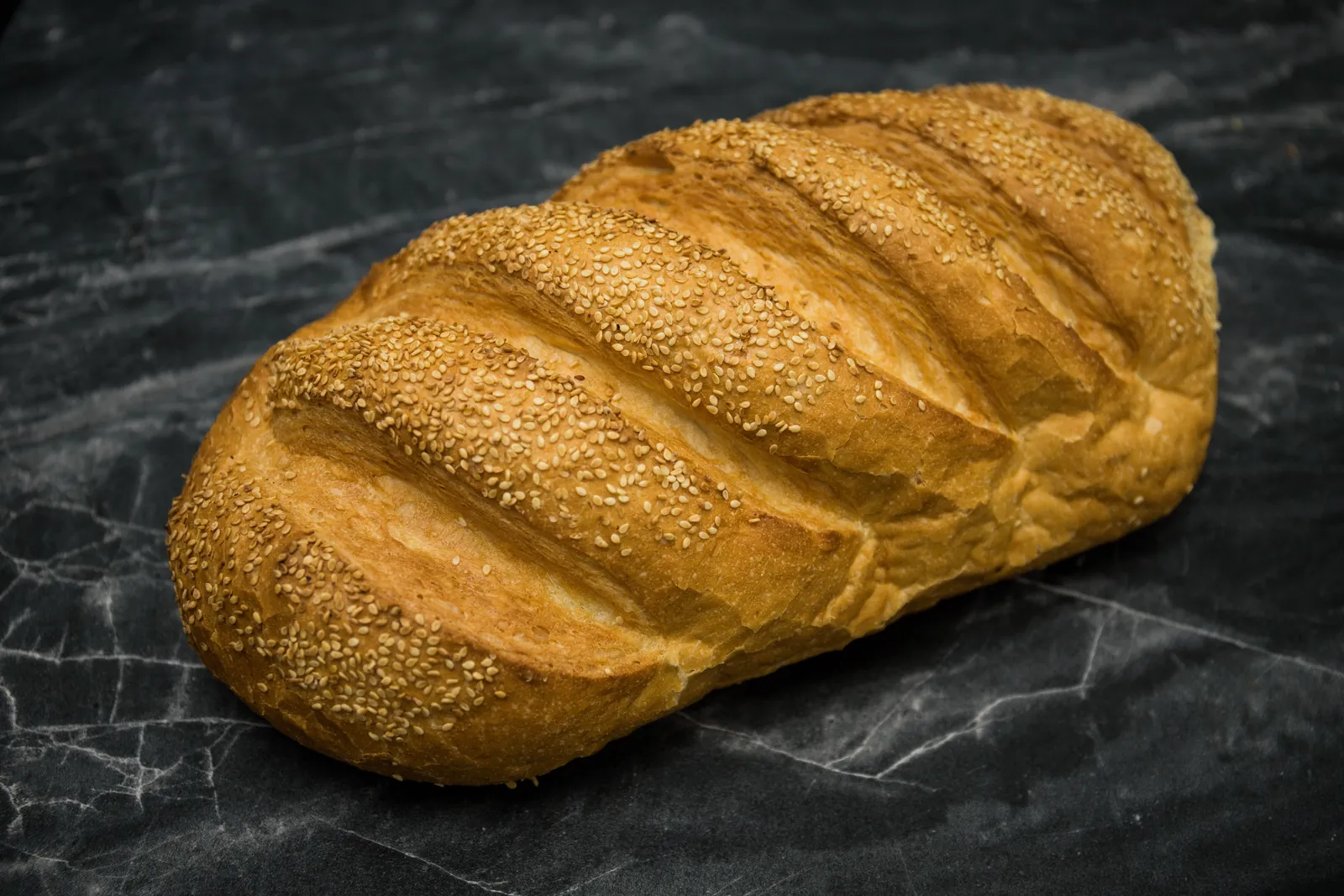 A sesame-topped white loaf on dark marble