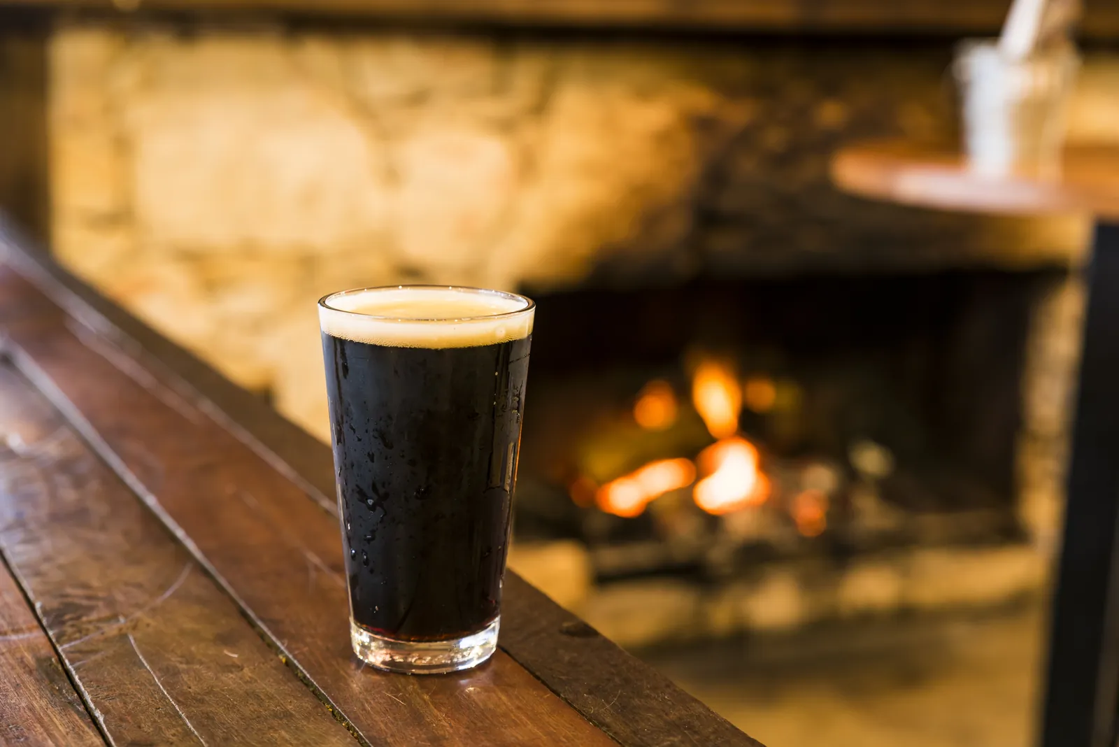A glass of dark beer on a timber ledge in front of the open fire at the Aireys Pub