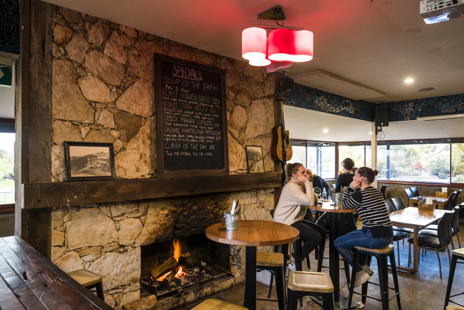 People at tables by the stone fireplace in the Aireys Pub, with the specials board above