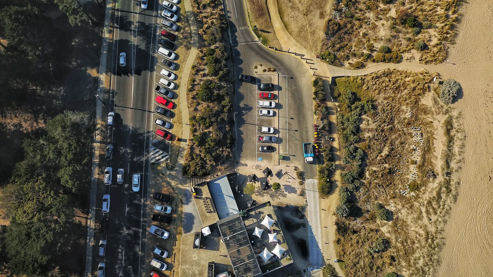 Looking straight down on the Salty Dog Cafe, its umbrellas and the Fishermans Beach car park, with the dunes and sand on the right