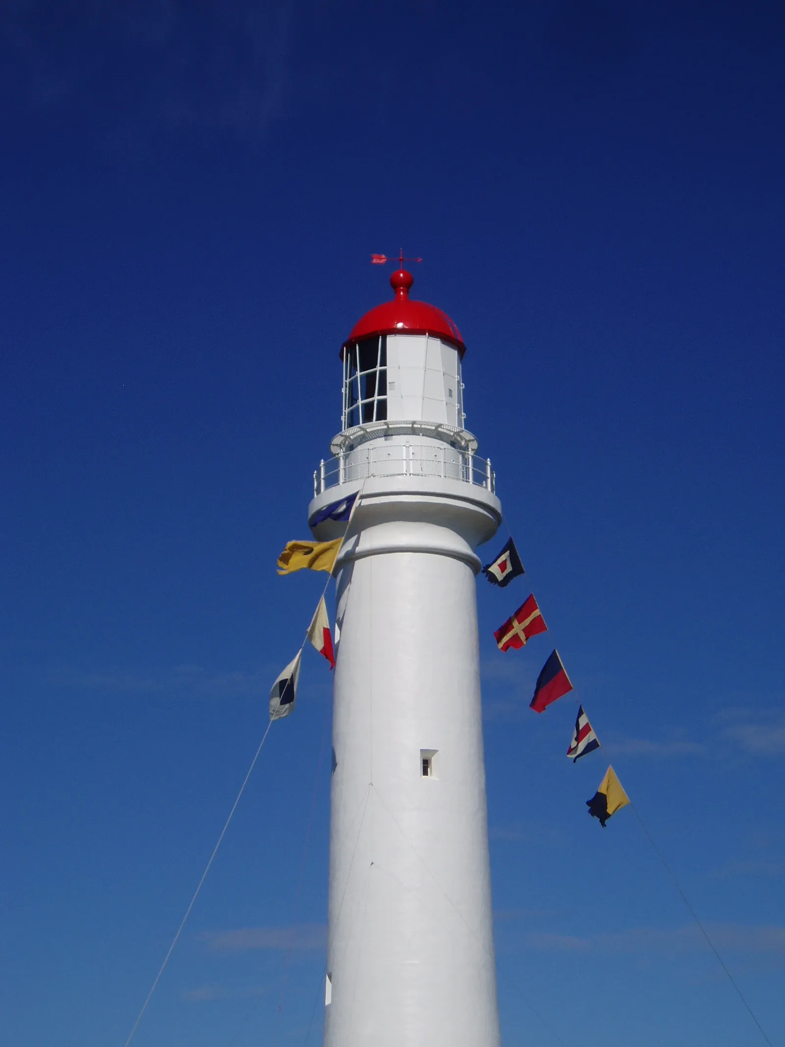 The white tower and red cap of Split Point Lighthouse, with signal flags against a blue sky