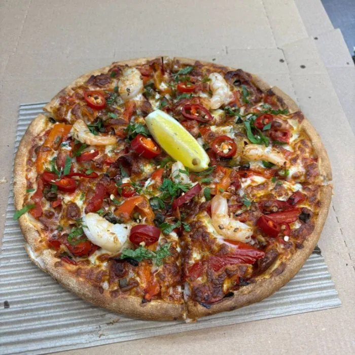 A prawn pizza with chilli, roast capsicum, herbs and a wedge of lemon