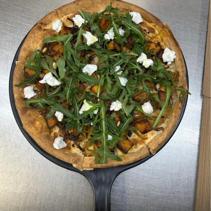 A pumpkin pizza topped with rocket, goat's cheese and pine nuts