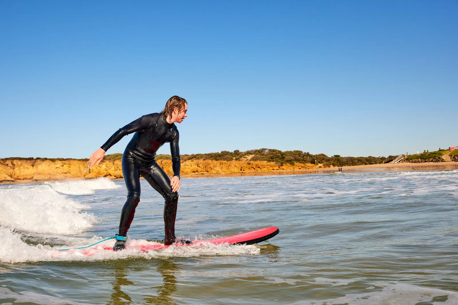 A surfer standing up on a soft-top board in the shallows at Torquay