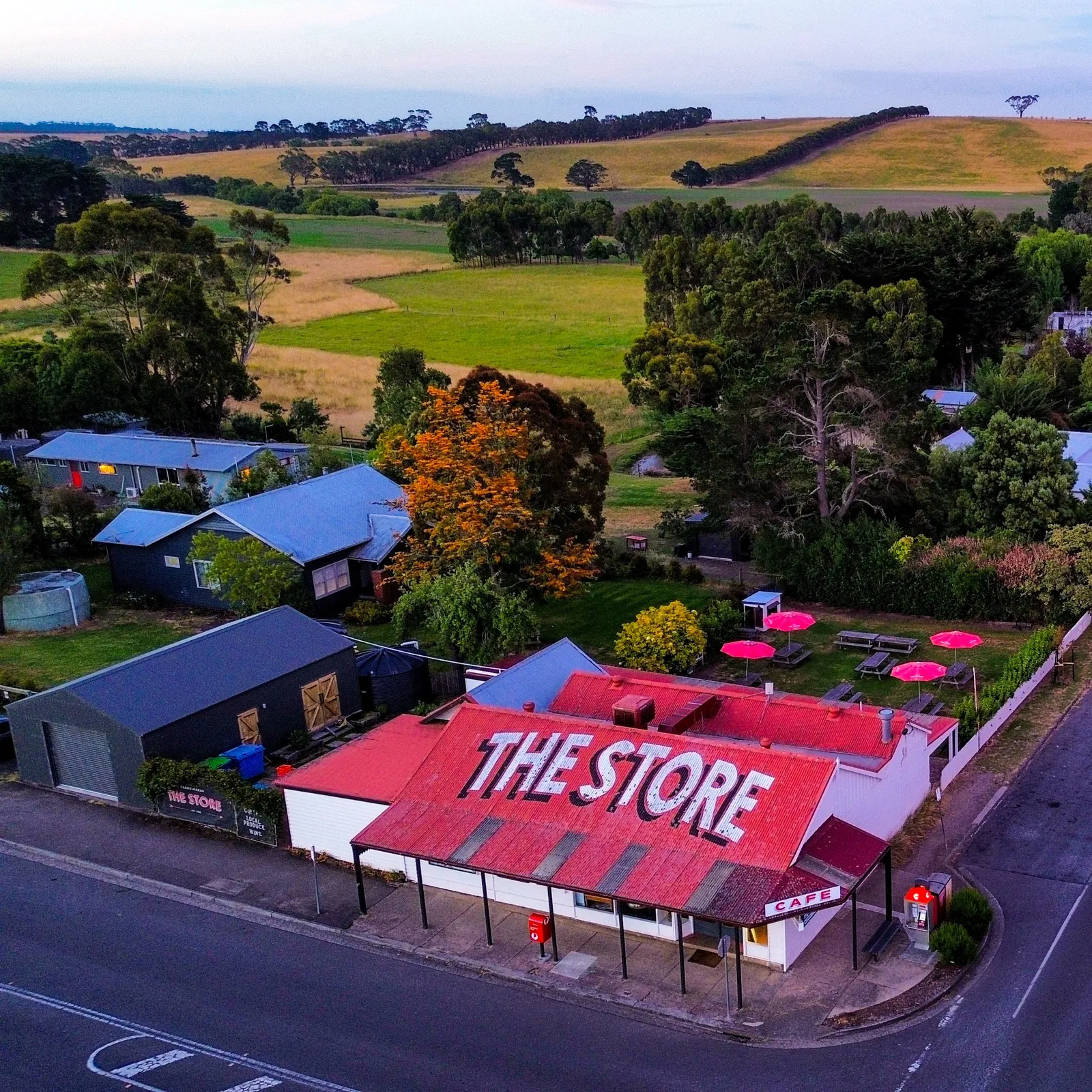 The Store from above at dusk, with pink umbrellas in the garden behind it and farmland rolling away beyond