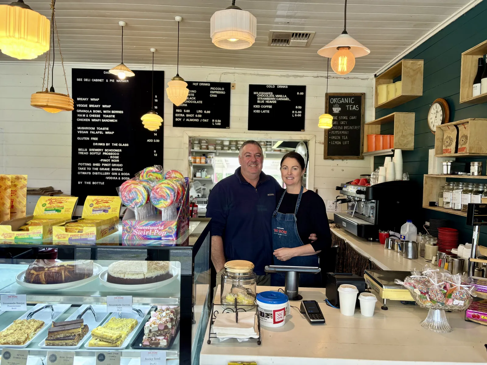 Dale and Jayne Stringer behind the counter at The Store, with the cake cabinet and blackboard menus