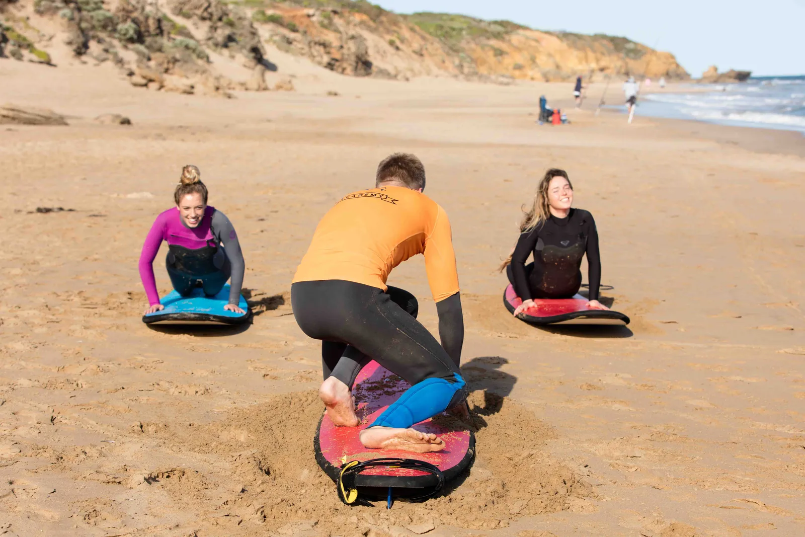 A Torquay Surfing Academy instructor showing two learners how to pop up on their boards on the sand