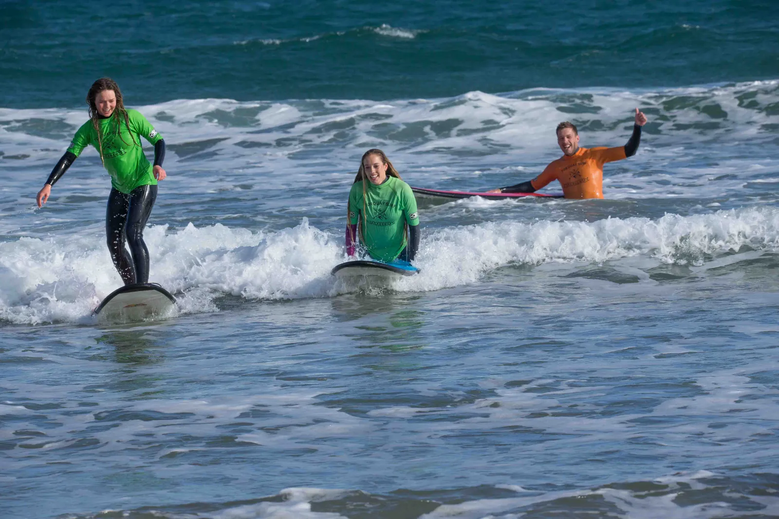 One learner standing up and another kneeling on a board in the whitewash, with an instructor cheering behind them