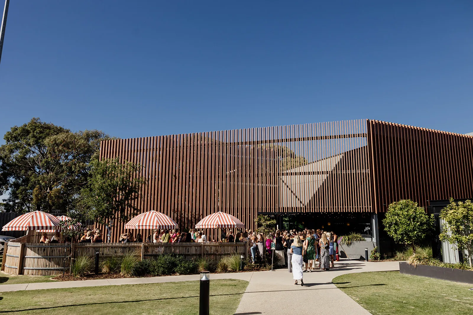 A crowd outside the timber-slatted Torquay Taphouse building, with striped umbrellas over the beer garden