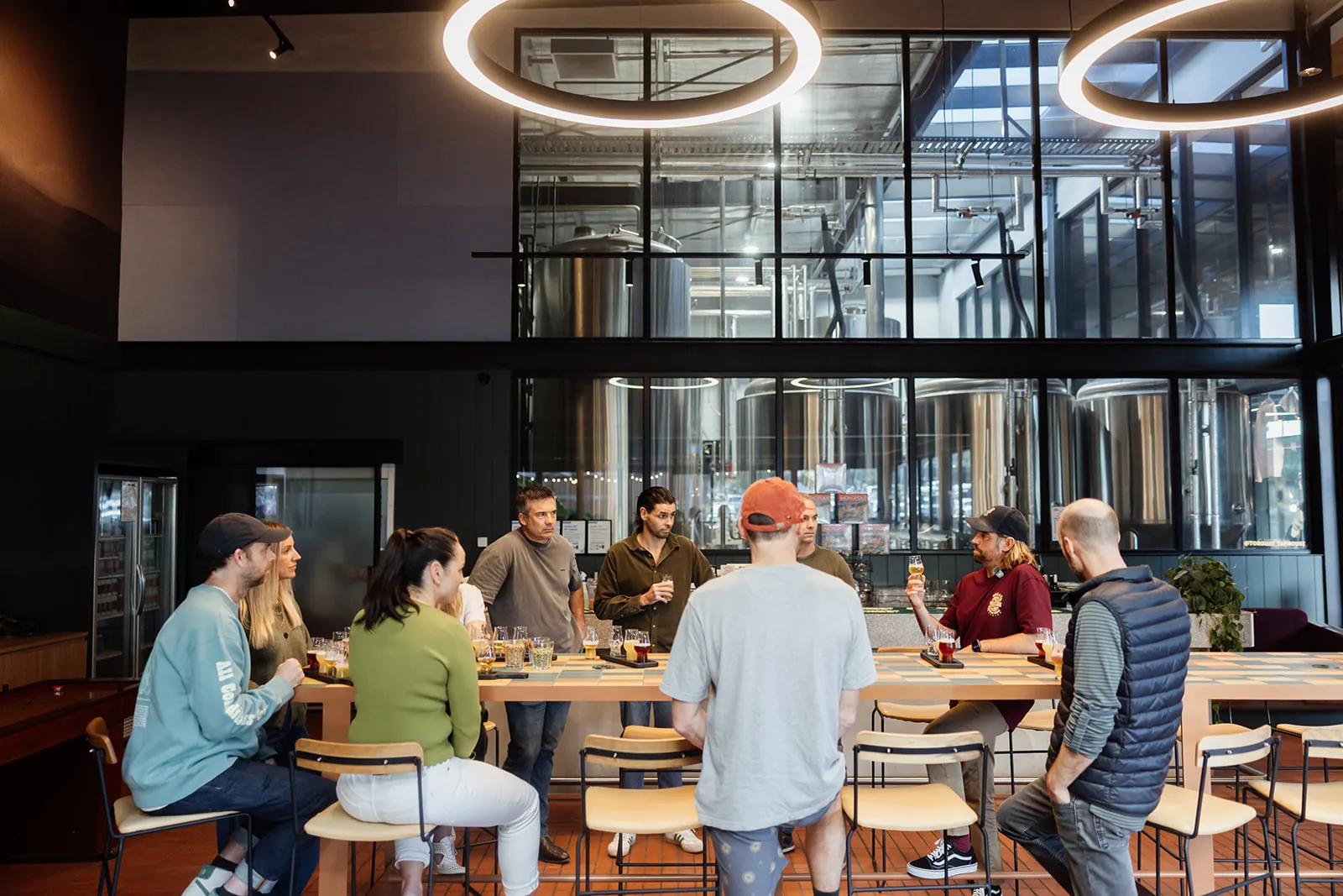 People tasting beer at a long table in the Torquay Taphouse, with the brewery tanks behind glass