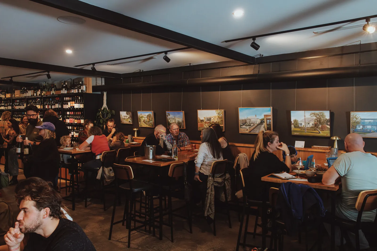 A busy evening at the tables inside Torquay Wine Store, with wine shelves along the walls