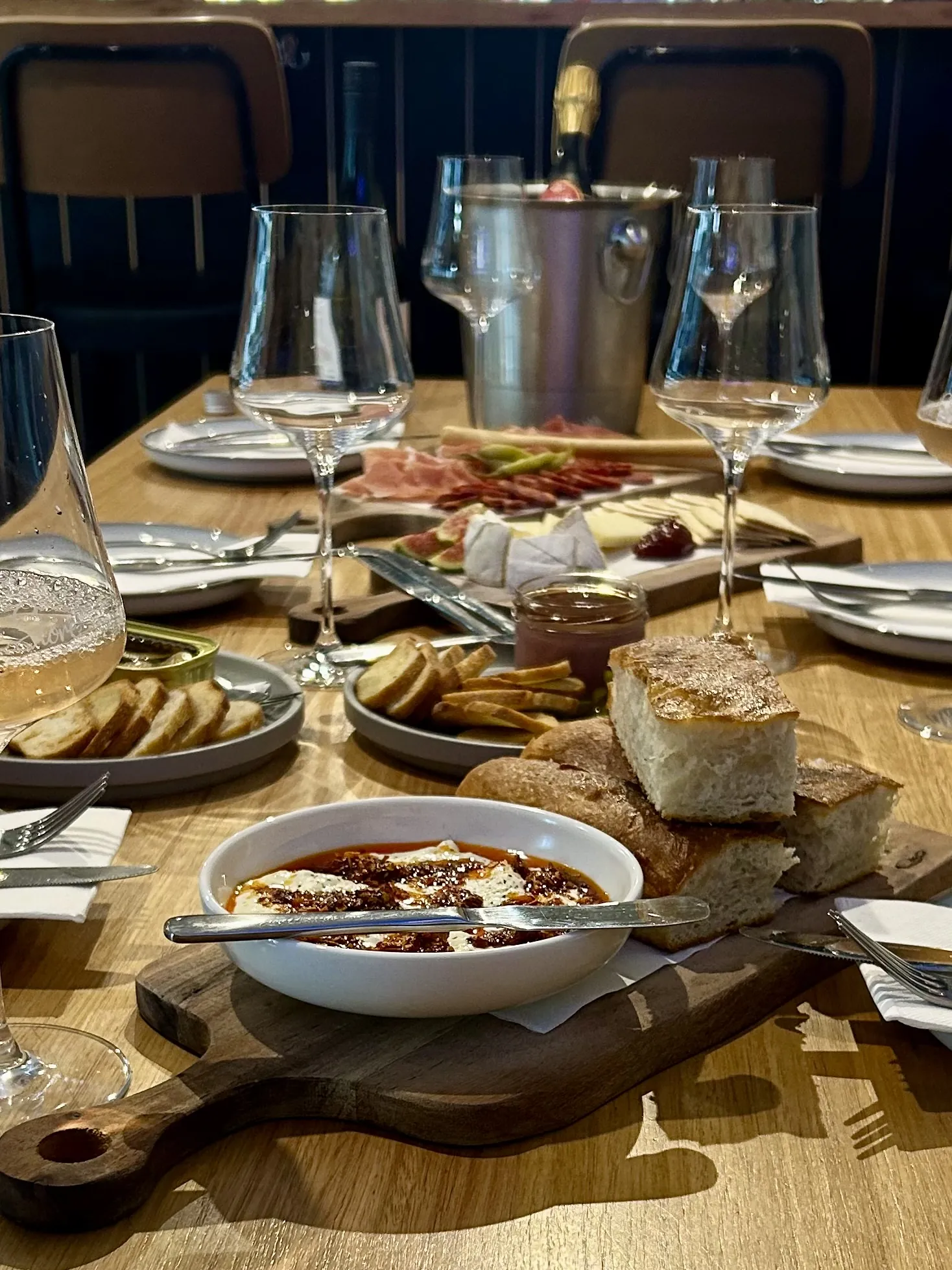 A grazing board of charcuterie, cheese and bread with a baked dip and wine glasses at Torquay Wine Store