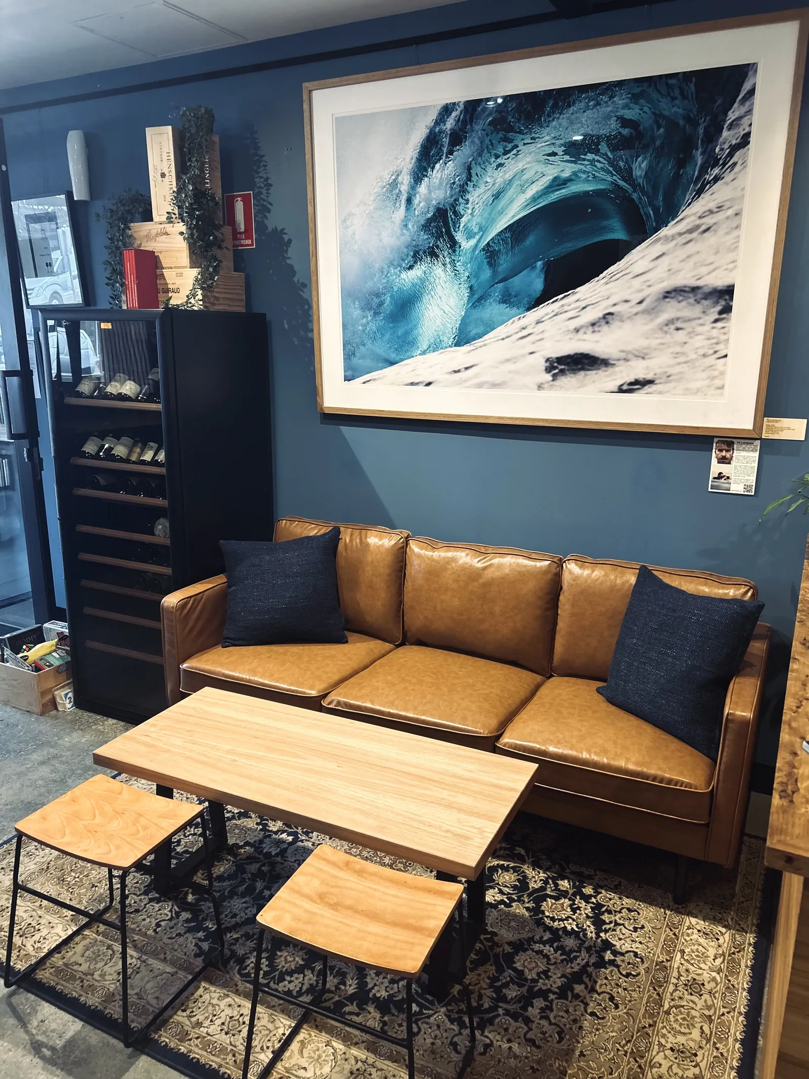 A leather couch and low table under a big wave photograph in a corner of Torquay Wine Store