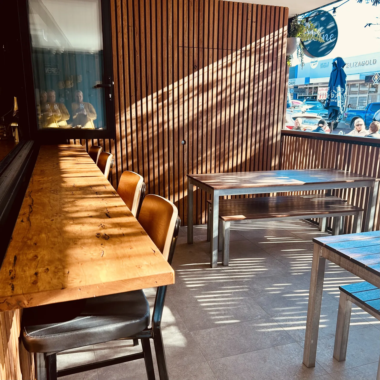 A long timber bench and chairs inside the front door of Torquay Wine Store, with the street beyond