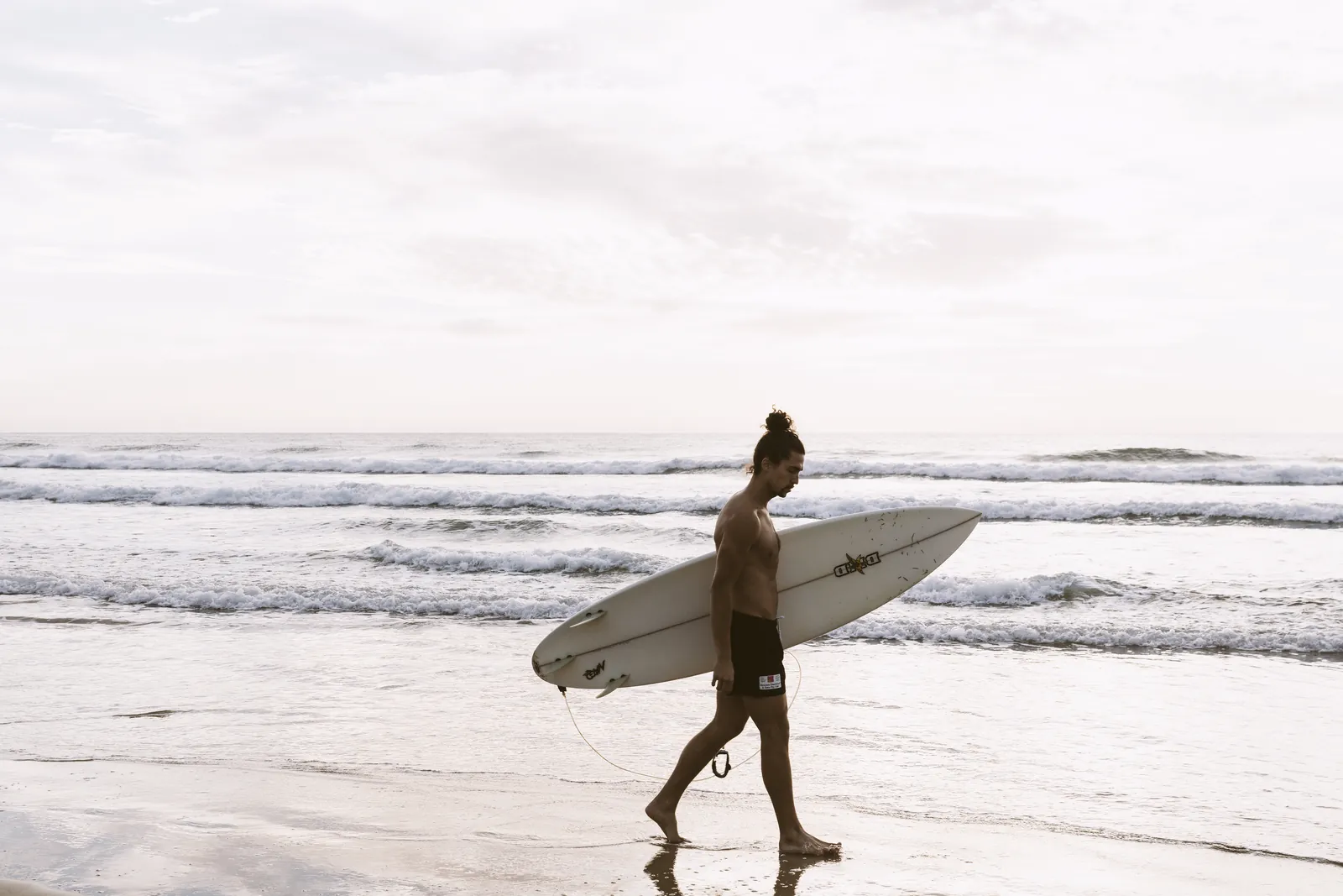 A surfer carrying a white surfboard across Wye River beach