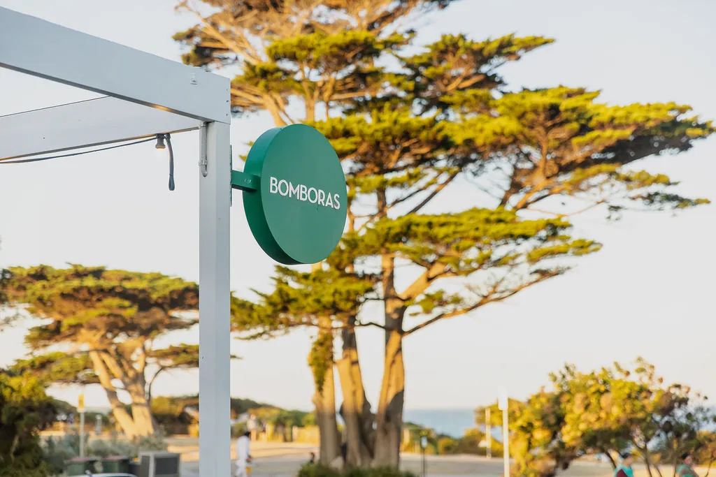 The round green Bomboras sign under the cypress trees on The Esplanade