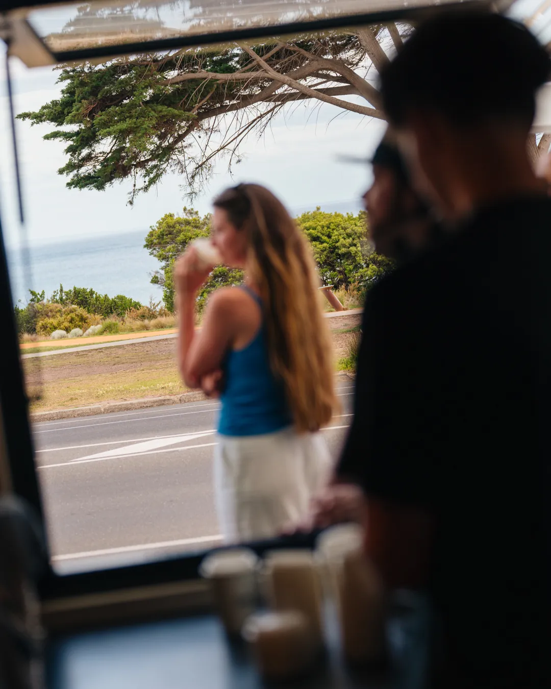 A guest by the window at Bomboras, with the cypress trees and sea behind