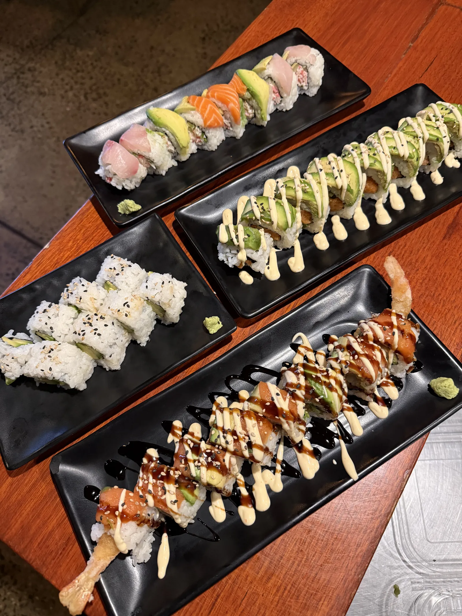 Four plates of sushi rolls at Roku Den, some topped with avocado and salmon, one with tempura prawn and drizzled sauces