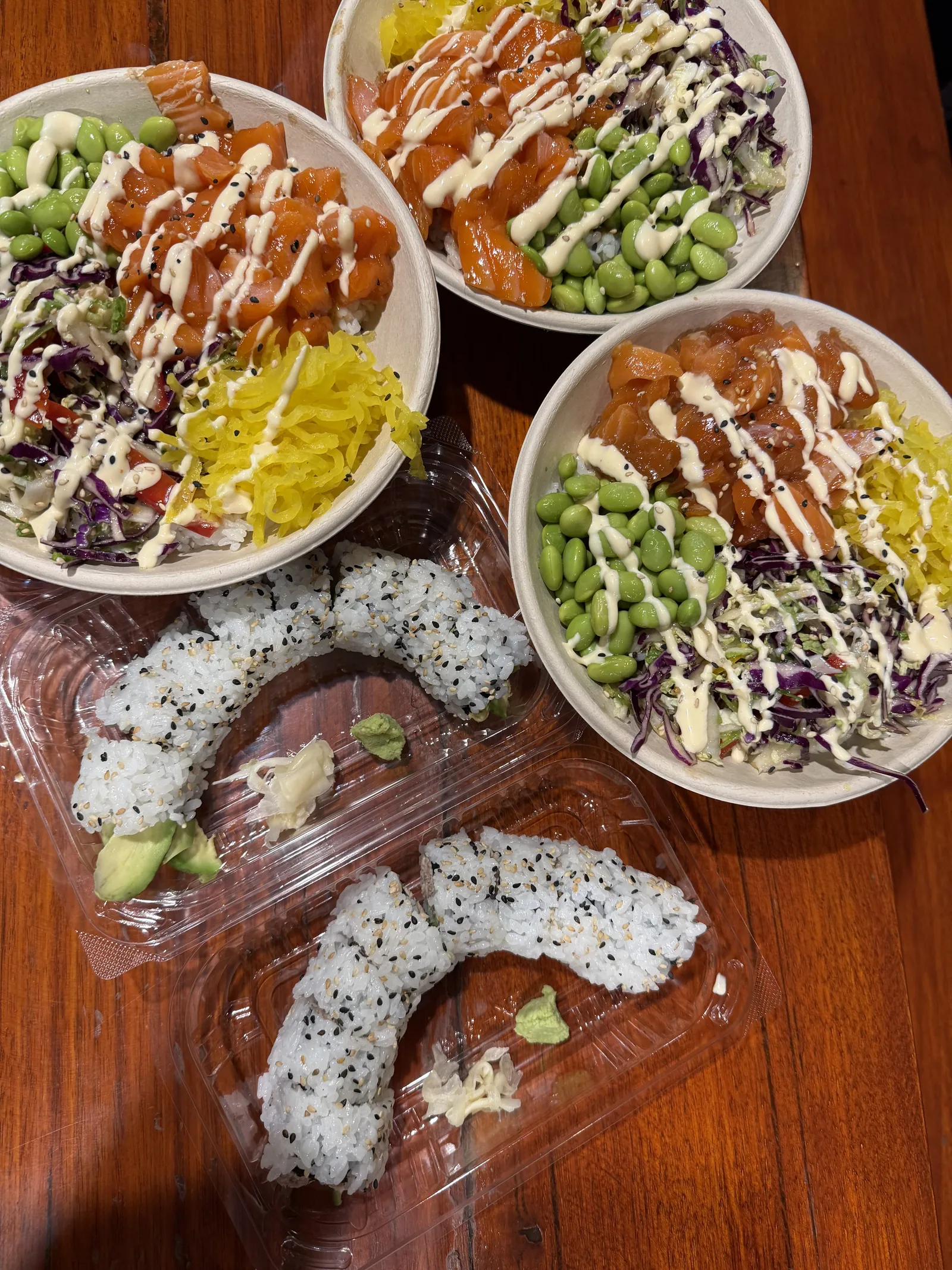 Salmon poke bowls with edamame, cabbage and pickled radish, and sushi rolls in takeaway trays, on a timber table at Roku Den