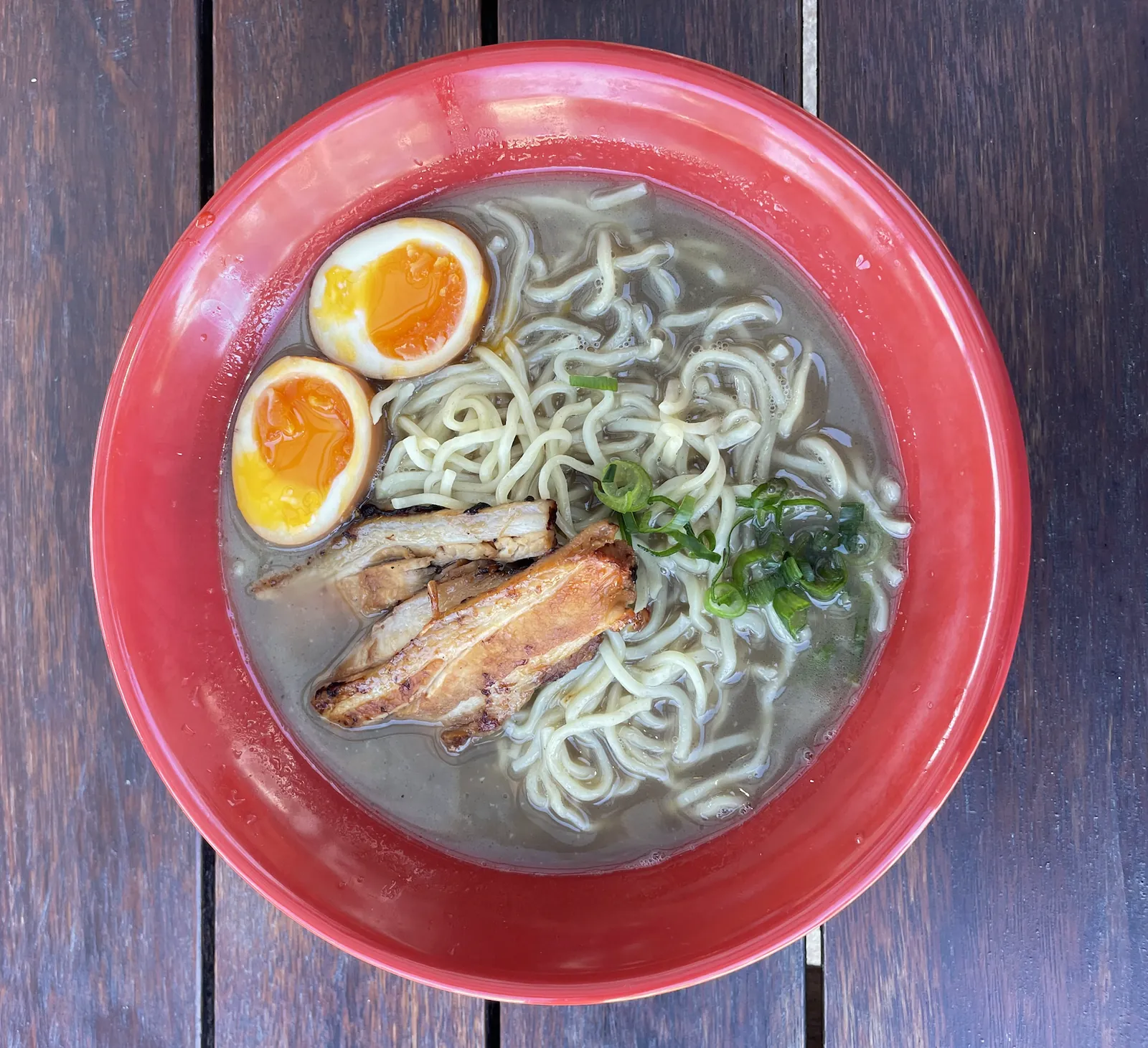 A red bowl of ramen at Roku Den with pork belly, a soft-boiled egg and spring onion