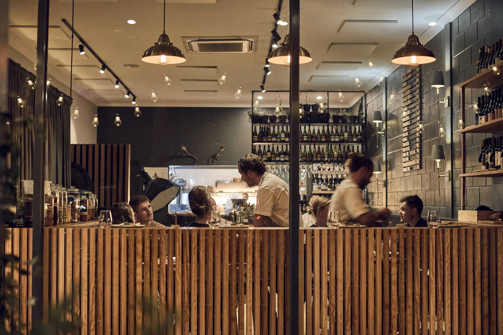 The Samesyn dining room seen through the timber screen, with chefs at the open kitchen and diners at the counter