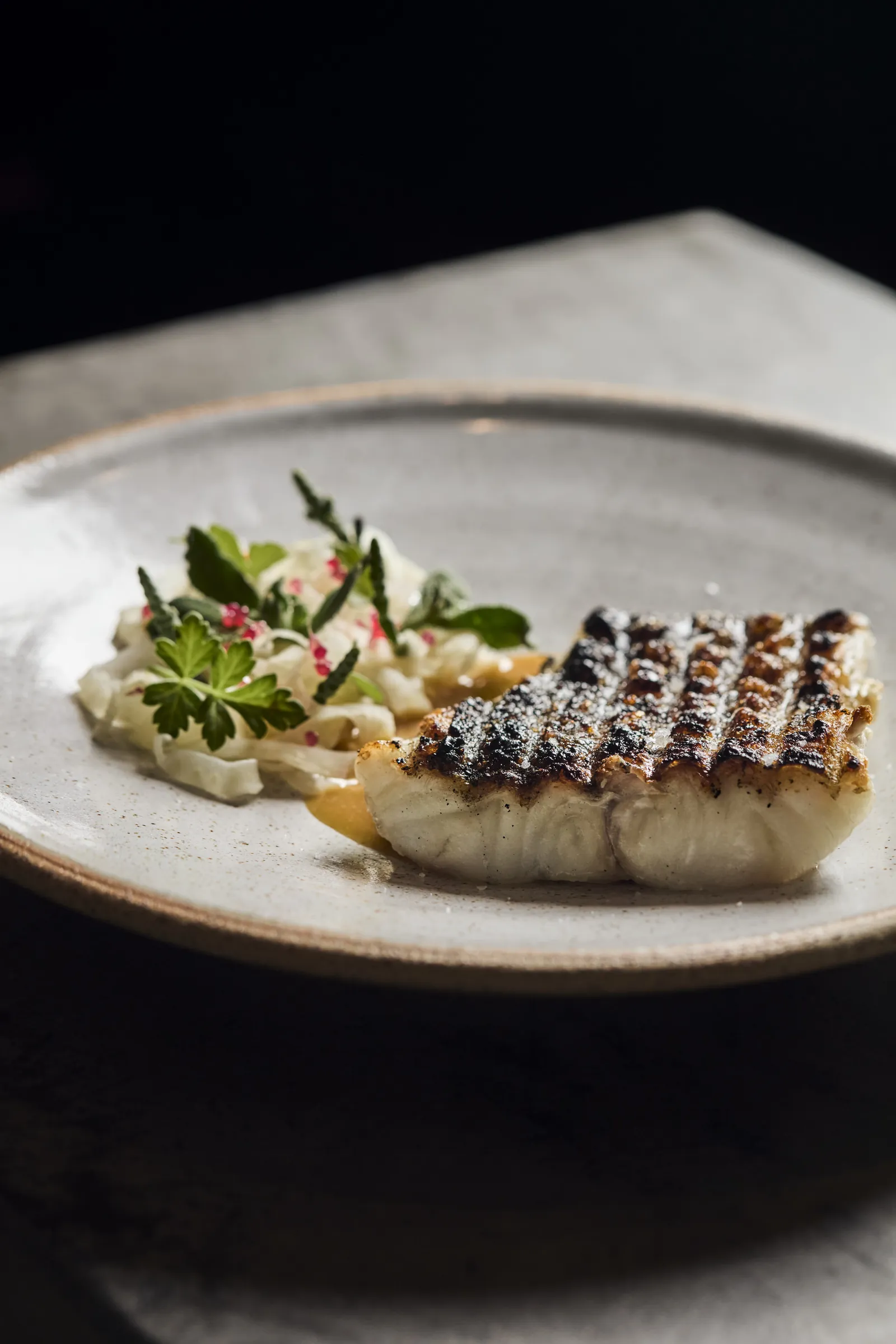 Grilled fish with a fresh herb salad on a grey ceramic plate