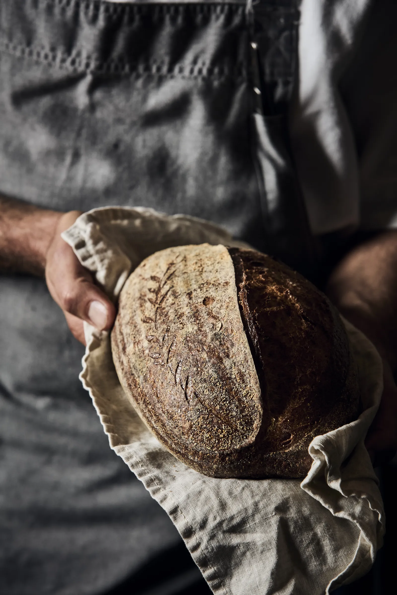 A chef holding a loaf of sourdough wrapped in a linen cloth
