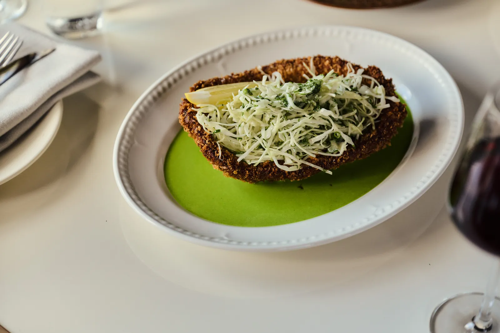 A schnitzel topped with slaw on a green sauce at Surf Hotel