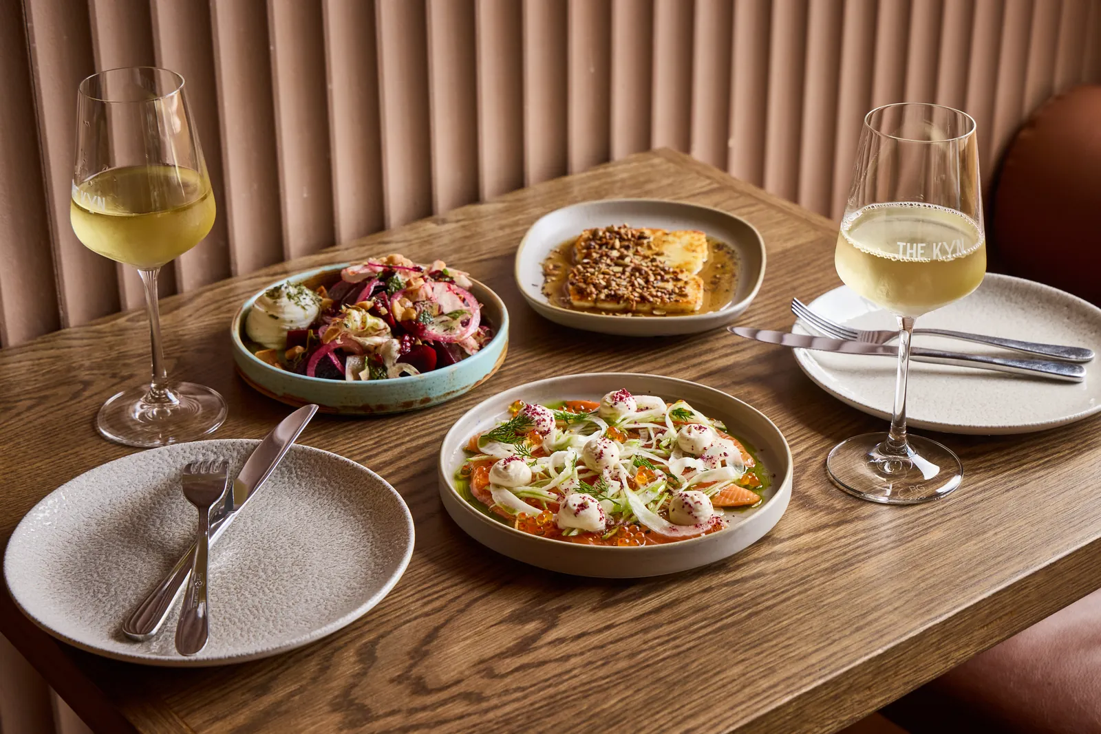 Share plates and white wine on a timber table at The Kyn