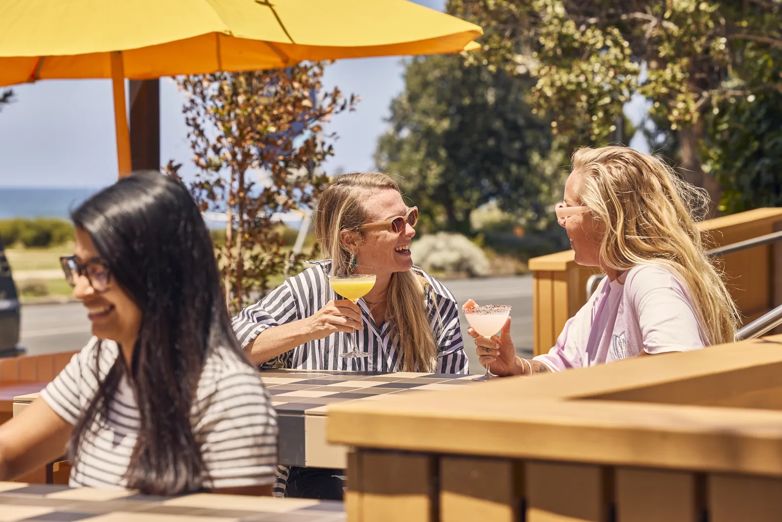 Friends with drinks under yellow umbrellas in The Kyn's front courtyard