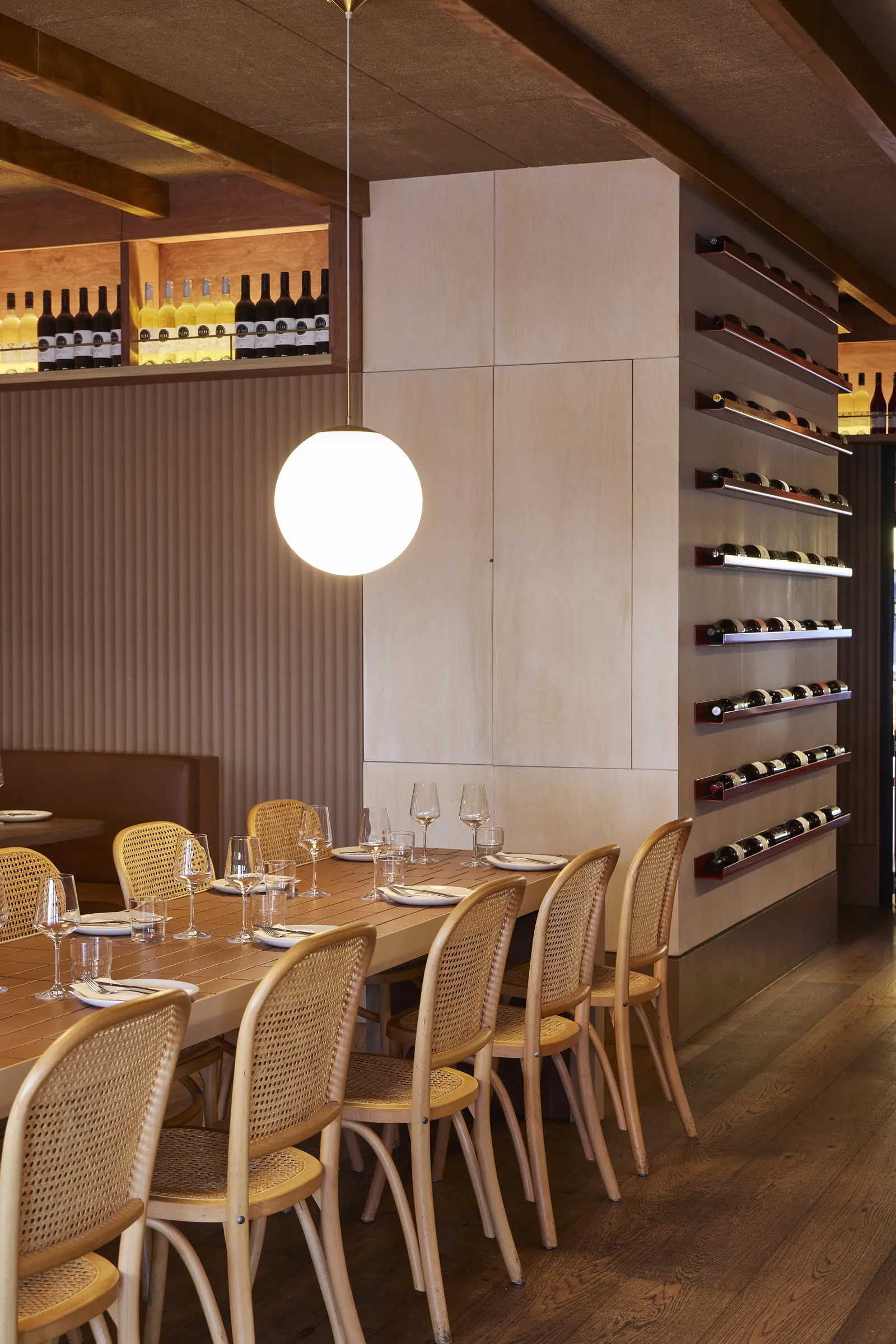 A long table with cane chairs beside the wine wall at The Kyn